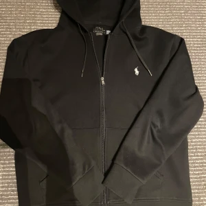 Svart hoodie från Polo Ralph Lauren - Säljer en stilren svart hoodie från Polo Ralph Lauren. Den har en dragkedja framtill och den klassiska loggan broderad på bröstet. Perfekt för både vardag och chill. Den är i mycket bra skick och passar till alla säsonger. Hör av dig vid intresse!