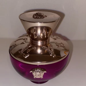Dylan Purple parfymflaska - Ny Säljer en lyxig parfymflaska från Versace, Dylan Purple. Flaskan är i en djup lila färg med eleganta silverdetaljer och Versaces ikoniska medusahuvud på locket. Perfekt för den som vill ha en stilren och exklusiv doft på hyllan.
