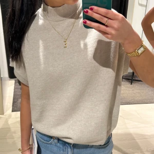 Beige stickad topp med polokrage - Snygg beige stickad topp med polokrage och korta ärmar. Är i mycket bra skick, inte alls noppig.