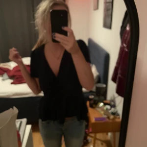 Mörkblå omlottopp - Säljer en snygg mörkblå omlottopp med korta ärmar. Toppen har en v-ringad design och en fin passform som markerar midjan. 