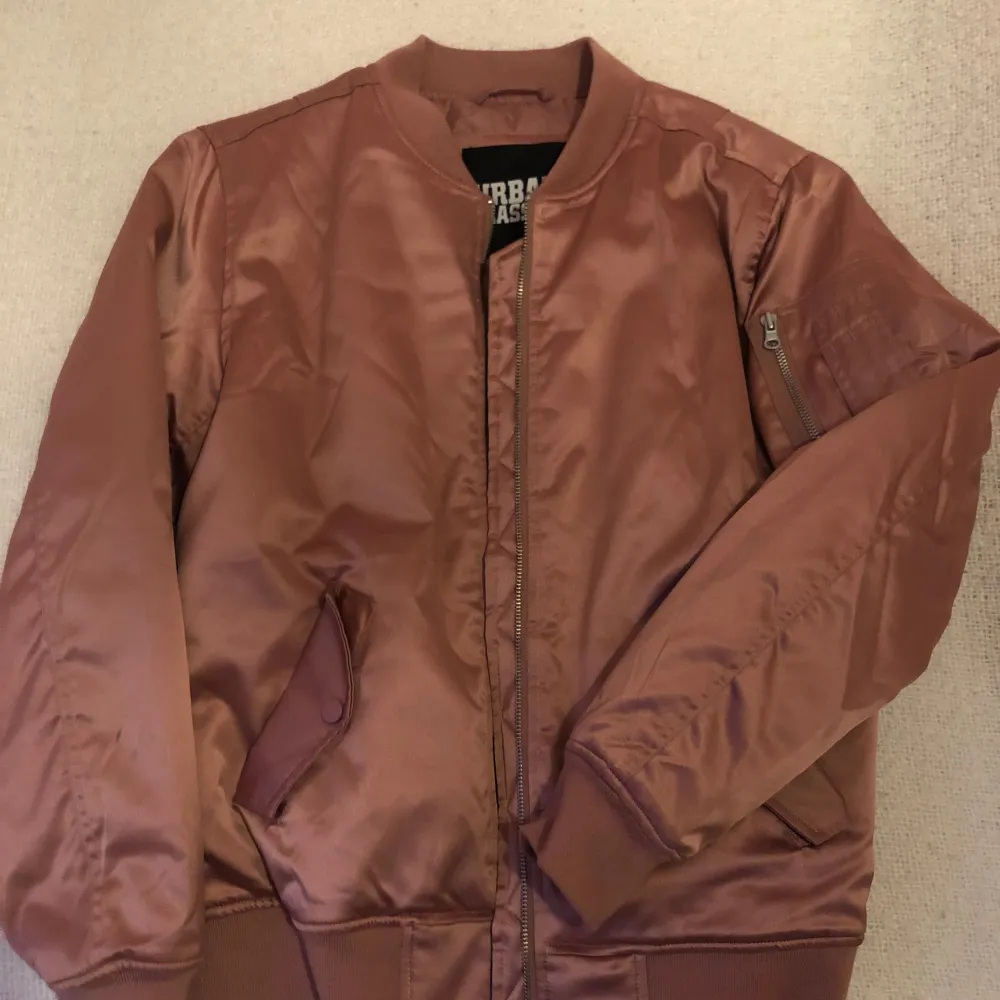 Säljer en snygg gammelrosa bomberjacka från Urban Classics. Jackan har en dragkedja framtill och en ficka med dragkedja på ärmen. Den är långärmad och perfekt för höst och vår. Passar både till vardags och fest!. Takit.