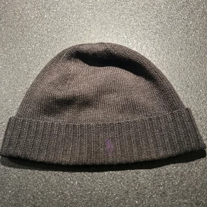 Grå mössa från Polo Ralph Lauren - Snygg grå mössa från Polo Ralph Lauren i stickat material. Den har en ribbad kant och en diskret broderad logga framtill. Perfekt för kyliga dagar.