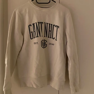 Vit sweatshirt från GANT - Säljer en stilren vit sweatshirt från GANT med tryck framtill. Tröjan har långa ärmar och ribbade muddar. Perfekt för en avslappnad stil.