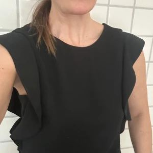 Svart klänning från Forever 21 - Elegant svart klänning från Forever 21 med volangdetaljer längs ärmarna. Perfekt för en stilren look. Strl. S men passar även en XS