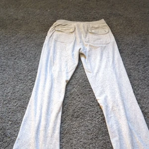 Grå mjukisbyxor med broderad logga storlek 12/13 år - Säljer ett par bekväma grå mjukisbyxor med broderad logga på framsidan. Byxorna har en loose passform och är utrustade med snörning i midjan för justerbar passform. Perfekta för en avslappnad stil.Finner ett litet hål i knäet men syns ej när de används