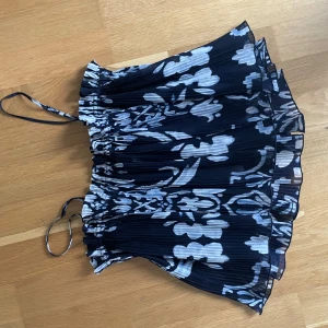 Blommig plisserad topp från H&M - Säljer en snygg blommig plisserad topp från H&M i marinblå och vit. Toppen har smala axelband och en elastisk överdel för en bekväm passform. Perfekt för varma sommardagar!