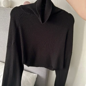 Svart stickad polotröja - Snygg svart stickad polotröja med croppad design. Perfekt för kyligare dagar med sin höga krage och långa ärmar. En stilren och trendig tröja som passar till många olika outfits. (den är brun på grund av ljuset annars är den hel svart!!) Storlek S/M