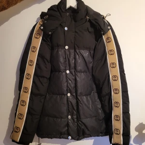 Svart dunjacka från Gucci - Snygg svart dunjacka från Gucci med beige detaljer längs ärmarna. Storlek S, sparsamt använd!  