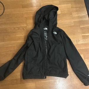 Svart regnjacka/windbreaker från The North Face - Säljer en knappt använd svart regnjacka från The North Face med huva och dragkedja. Jackan är perfekt för regniga dagar och har en stilren design. Den är tillverkad i ett lätt och slitstarkt material. Dessa typer av jackor används ofta i huligan relaterade aktiviter