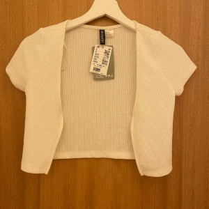 Bolerotopp - Säljer vit ribbad bolerotopp från h&m. Helt ny och oanvänd med prislapp. Toppen har korta ärmar och är öppen framtill, perfekt för lager-på-lager❤️Passar utmärkt till både vardag och festliga tillfällen.