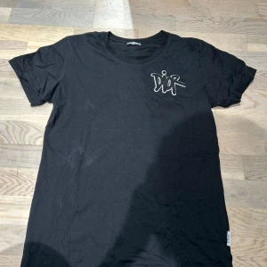 Dior T-shirt med tryck - Snygg svart t-shirt från Dior med en broderad logga på bröstet. Perfekt för en stilren och modern look. T-shirten har en klassisk passform och är kortärmad. Storlek S