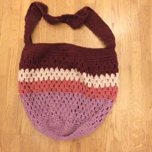 Virkad väska - Charmig virkad väska i flera färger: vinröd, beige, rosa och lila. Perfekt för en bohemisk stil med sitt luftiga mönster och breda axelrem. Väskan är rymlig och passar utmärkt för vardagsbruk.  Längd utan axelrem: 37cm Omkrets: 75cm Axelrem: 75x6 cm Bomull