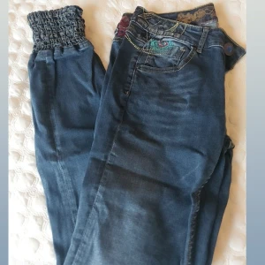 Blå jeansbyxor från Desigual - Snygga blå jeansbyxor från Desigual med unika detaljer. Byxorna har en elastisk midja och dekorativa sömmar. Perfekta för en avslappnad stil.