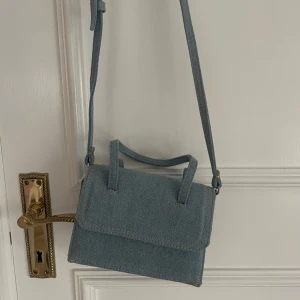Blå axelväska i jeansmaterial från Zara - Snygg blå axelväska i jeansmaterial med justerbar axelrem. Perfekt för en avslappnad stil och passar till många olika outfits. Väskan har ett enkelt och stilrent utseende.