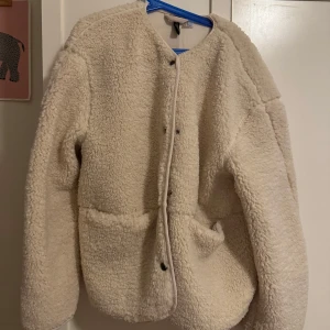 Beige teddyjacka -  beige teddyjacka med knappar framtill. Jackan har en rund halsringning och två praktiska fickor. Den är i storlek XS men är oversized (jag brukar ha S-M)