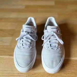 Grå sneakers från Adidas - Snygga grå sneakers från Adidas med klassisk design och snörning. Skorna har en vit sula och är i bra skick. Perfekta för en stilren och bekväm look.