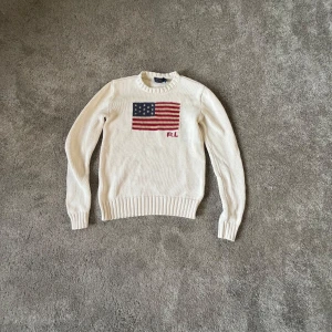 Vit stickad tröja från Polo Ralph Lauren - Snygg vit stickad tröja från Polo Ralph Lauren med amerikanska flaggan på framsidan och broderi. Amerikanska flaggan har ändrat färg lite.