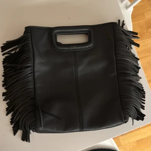Svart väska med fransar från Maje - Sjukt snygg väska från Maje med fransar på sidorna. Kommer med avtagbar kedja och dustbag. Tror det är storlek M eller L. Skriv för mer bilder och info. Bra skick förutom att märket skrapats bort litegrann, men inget man tänker på. Inte säker på att jag vill sälja men kom med prisförslag!💗