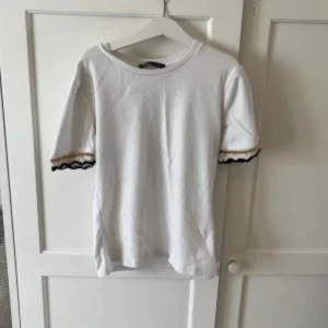 Vit t-shirt med guldiga och svarta detaljer  - Jättefin T-shirt med snygga detaljer endast använd någon gång.💕 