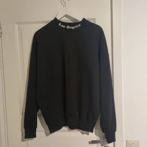 Svart sweatshirt med Los Angeles-tryck - Säljer en svart sweatshirt med texten 'Los Angeles' i vitt på både framsidan och baksidan. Tröjan har långa ärmar och en rund halsringning. Perfekt för en avslappnad stil. Oversize