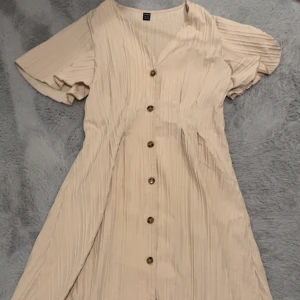 Klänning - Så fin klänning som är figursydd i midjan och mer utsvängd i armarna och längst ner. Mer beige i verkligheten. 