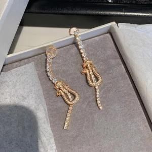 Guldglittriga örhängen med strass - Eleganta guldörhängen dekorerade med glittrande strass. De har en unik design med en böjd form och hängande detaljer som ger en lyxig känsla. Perfekta för att lysa upp vilken outfit som helst.