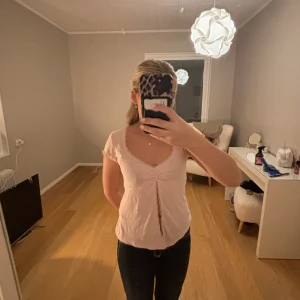 Ljusrosa topp  - Söt ljusrosa topp från Gina tricot med korta ärmar och rynkdetalj framtill. Toppen har en v-ringad hals och är tillverkad i ett mjukt material som ger en bekväm passform.