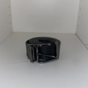 Emporio armani bälte - Säljer ett stilrent svart skärp i skinn med ett snyggt silverfärgat spänne. Finns två sidor på den som man ser. Gjorde extra hål för passade inte mig där av priset, Skärpets storlek är nog Xl men finns extra hål om man är mindre.