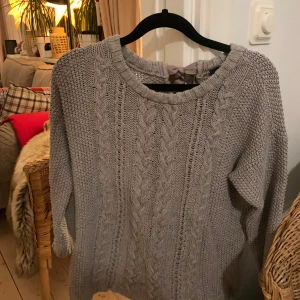 Grå stickad tröja från Oui - Mysig grå stickad tröja från Oui med kabelstickat mönster och en söt rosett i nacken. Aldrig använd. Storlek står itne på men skulle säga S/M