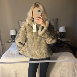 Beige/grå pälsjacka - Säljer denna snygga pull over pälsjacka. Jackan har en fluffig och varm design med långa ärmar. Super skön men säljer då den inte kommer till användning.