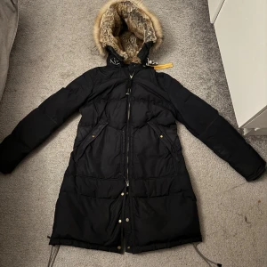 Svart dunjacka med pälsdetaljer från Parajumpers - Säljer en svart dunjacka från Parajumpers med avtagbar huva och pälsfoder. Jackan har dragkedja och knappar framtill samt flera praktiska fickor. Perfekt för kalla vinterdagar. Pris kan även diskuteras!
