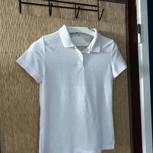 Vit pikétröja - Säljer en klassisk vit pikétröja med krage och knappar. Perfekt för en stilren och avslappnad look. Tröjan är kortärmad och gjord i ett bekvämt material. Köpt på secondhand så märke saknas.