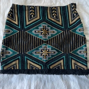 Mönstrad kjol med fransar - Säljer en supersnygg kjol med mönster i svart, grönt och guld🤗. Kjolen har en tight passform och har fransar längst ner. Perfekt för en fest eller en utekväll! Baksidan är helt svart och den är i superfint skick💕💕