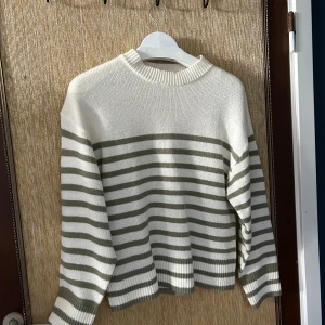 Randig stickad tröja - Säljer en superfin stickad tröja med vita och gröna ränder. Den är perfekt för höst och vinter, och är riktigt mysig och varm. Tröjan har långa ärmar och en normal passform. Perfekt för att hålla sig varm under kyliga dagar!