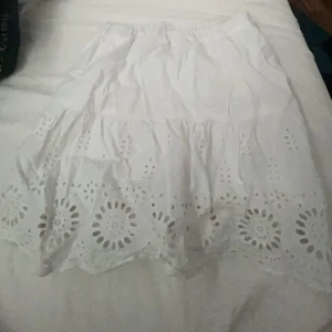 Vit kjol med broderade detaljer - Säljer en supersöt vit kjol med vackra broderade detaljer längst ner. Kjolen har en elastisk midja för en bekväm passform och är perfekt för sommardagar. Den är gjord i ett lätt och luftigt material, vilket gör den idealisk för både vardag och fest. Passar perfekt till en enkel topp eller blus! Mycket bra skick och är från kappahl, storlek 146.