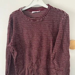 Vinröd och vit randig tröja - Säljer en vinröd och vit randig tröja i storlek M. Tröjan är långärmad och har en rund halsringning. Perfekt för höst och vinter, den är både bekväm och stilren. Passar bra till både vardag och avslappnade tillfällen.