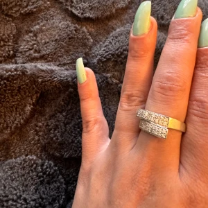 Silver ring med glittriga stenar - Säljer en snygg ring i äkta silver med glittriga stenar. Ringen har en modern design med två parallella band som är täckta av små gnistrande stenar. Perfekt för att lägga till lite extra bling till din outfit! 💍✨