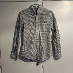 Rutig skjorta från Ralph Lauren - Säljer en snygg rutig skjorta från Ralph Lauren i storlek S. Skjortan är slim fit och har ett klassiskt rutmönster i svart och vitt. En av knapparna är utbytt. skick 6/10. Frågor och funderingar? Tveka inte på att höra av dig.