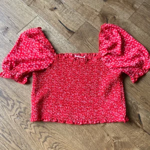 Röd blommig topp från NA-KD - Säljer en superfin röd topp från NA-KD med små vita blommor. Toppen har puffiga kortärmar och en smockad design som ger en tight passform! 