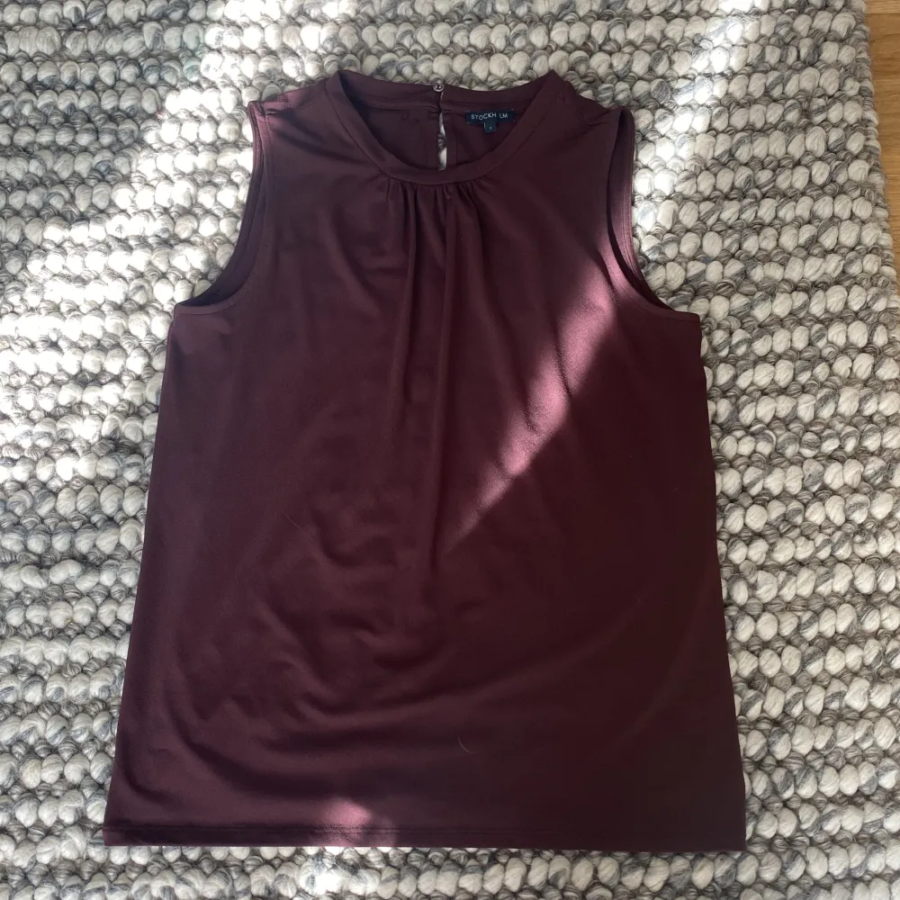Säljer en stilren vinröd ärmlös topp från Stockh LM i storlek S. Toppen har en enkel design med rund halsringning och är perfekt för både vardag och fest. Materialet känns mjukt och bekvämt mot huden.. Yläosat.