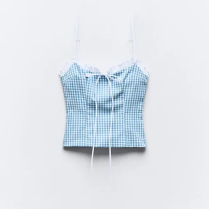 Blå och vit rutig linnetopp med spetsdetaljer - Säljer en superfin blå och vit rutig linnetopp med justerbara axelband. Toppen har söta spetsdetaljer vid halsringningen och en knytning framtill. Perfekt för sommardagar på stranden eller en avslappnad dag ute. Materialet är lätt och bekvämt, vilket gör den idealisk för varma dagar. Toppen är i nyskick och har bara använts ett fåtal gånger.