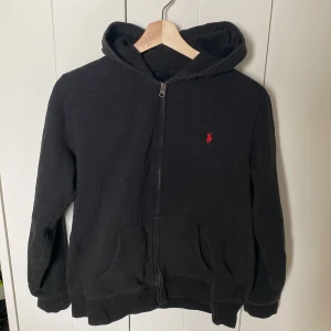 Polo Ralph Lauren Zip Hoodie - Svart Polo Ralph Lauren Zip hoodie i str XL barn (18-20år). Jag är en M dam och den sitter fint på mig (bild 3). Den är lite använd men färgen har släppt lite så den är inte mörkt svart längre.