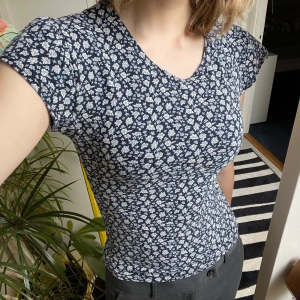 Blommig topp från Spell - Säljer en superfin blommig topp från Spell. Den är mörkblå med små vita blommor och har en tight passform. Den har blivit formsydd så midjan är insydd medans ärmarna är avkortade 💙