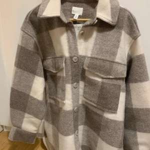 Rutig overshirt från H&M - Säljer en superfin rutig overshirt från H&M i beige och grått. Den har en skön och lite oversized passform med långa ärmar och knappar framtill. Perfekt för höst och vår när man vill ha något stilrent och bekvämt. Två stora fickor på bröstet ger en cool look. Passar både till vardags och lite mer uppklädda tillfällen!