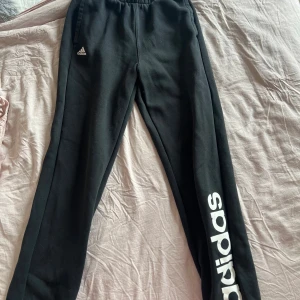Svarta mjukisbyxor från Adidas - Säljer ett par svarta mjukisbyxor från Adidas. De har en elastisk midja och är superbekväma för både träning och chill. Adidas-loggan syns tydligt på benet, vilket ger en sportig look. Perfekta för höst och vinter!