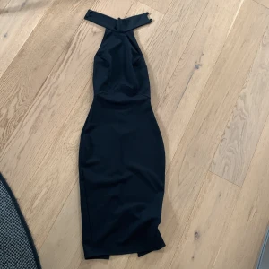 Svart klänning från NLY One - Säljer en elegant svart klänning från NLY One i storlek XS. Klänningen har en stilren design med en hög krage och knappar i nacken. Den är ärmlös och har en tight passform som framhäver figuren. Perfekt för festliga tillfällen!