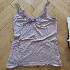 Beige linne med rosett - Säljer ett sött beige linne från mango i storlek s! med lila spetsdetaljer och en liten lila rosett framtill. 