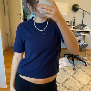 Mörkblå croppad t-shirt - Säljer en snygg mörkblå croppad t-shirt i bomull. Den har en enkel design med korta ärmar och en bekväm passform. Perfekt för sommardagar eller som en del av en lager-på-lager-look. Passar bra till både jeans och kjol!