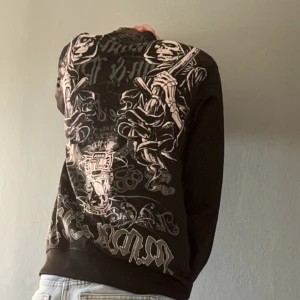 Svart hoodie med tryck -  svart zip med detaljerat tryck på ryggen och en mindre design på framsidan. 