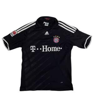 Säljer en svart Bayern München fotbollströja från Adidas med Ribéry och nummer 7 på ryggen. Tröjan har korta ärmar och vita detaljer, inklusive klubbens emblem och sponsorlogga på framsidan. Perfekt för fans av Bundesliga och Bayern München!